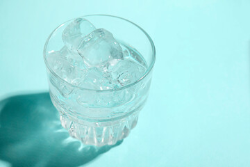 Refreshing water with ice in glass on turquoise background, closeup. Space for text