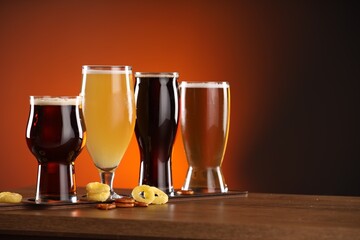 Glasses with different types of beer on wooden table against color background, space for text