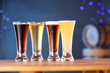 Glasses with different types of beer on wooden table against blue background, closeup
