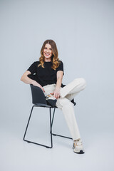 A pretty woman in a black t-shirt and white pants on a white background. Smiling woman in casual clothes on a white background.