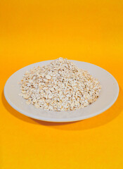 oat, oat grains, oat flakes in a white plate, isolated on yellow background and close up shot.