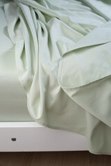 A light green cotton sheet lying carelessly on the bed. Close-up, macro photo. Minimalist bedroom....