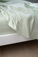 A light green cotton sheet lying carelessly on the bed. Close-up, macro photo. Minimalist bedroom. Cozy home concept. Scandinavian style