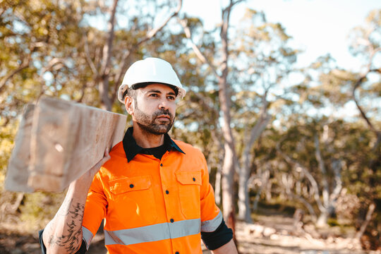 A bearded contractor carrying a timber on his shoulder.
