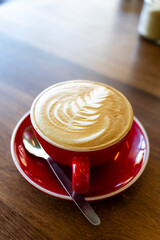 cup of cappuccino in a red cup on wood table close up