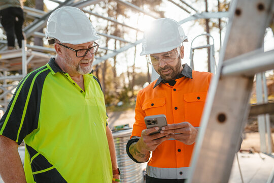 Two men wearing safety gears on the site with one holding a mobile device.