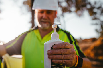 Construction worker on a blurry background holding sunscreen pump bottle