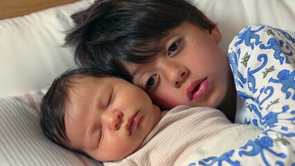 Sweet and tender moment as an older brother kisses his sleeping newborn sibling on the forehead, both lying on a bed, wrapped in warmth and love