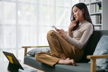 A woman is sitting on a couch with a tablet in her lap