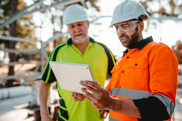 Two construction site managers looking at digital blueprints on tablet device
