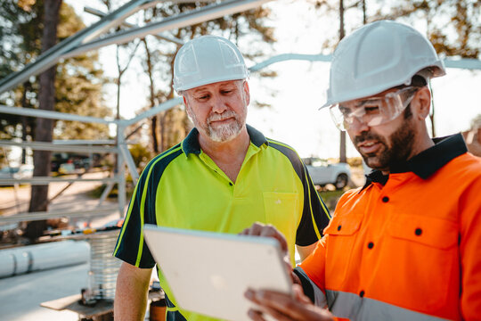 Two construction site managers looking at digital blueprints on tablet device