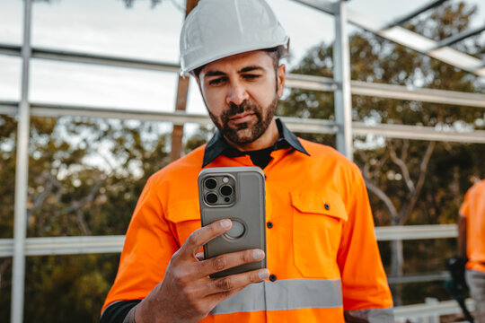 A bearded man holding a mobile phone in the construction site.