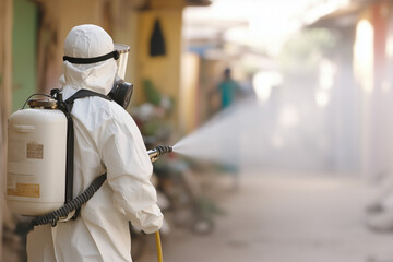 Healthcare worker in protective gear, using a fogging machine to spray chemicals in an open community area, fog billowing as part of a mosquito elimination campaign.