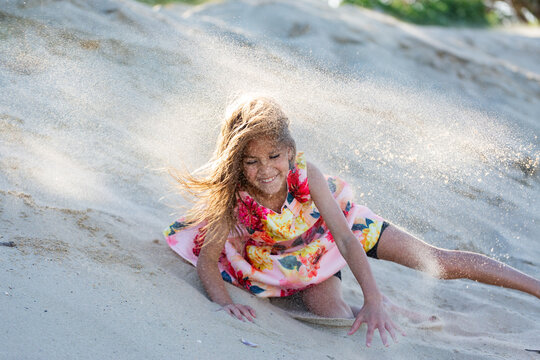 First Nations Australian Torres Strait Islander kid rolling down sand dune at the beach