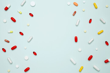 Various colorful pills and capsules scattered on a light blue background. Concept of medicine, healthcare, and pharmaceutical industry