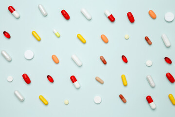 Various colorful pills and capsules scattered on a light blue background. Concept of medicine, healthcare, and pharmaceutical industry