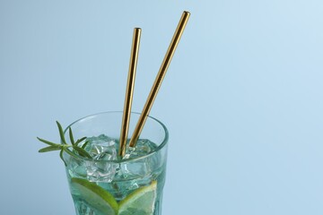 Tasty refreshing drink with straws in glass on light blue background, closeup. Space for text
