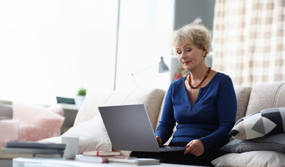 Portrait of senior woman learn how to use modern laptop device at home on sofa. Aging female...