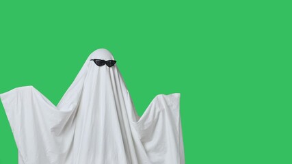 Funny halloween ghost in white sheet wears black glasses dancing coolly, isolated on chroma key green screen background. Happy halloween spooky concept.