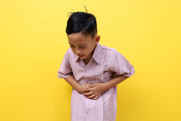 Asian little boy standing while grimacing in pain. He is suffering from stomach ache or diarrhea