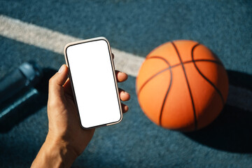 Smartphone in hands basketball player during game interval. Blank screen. Sports mock up. View from above. Close up.