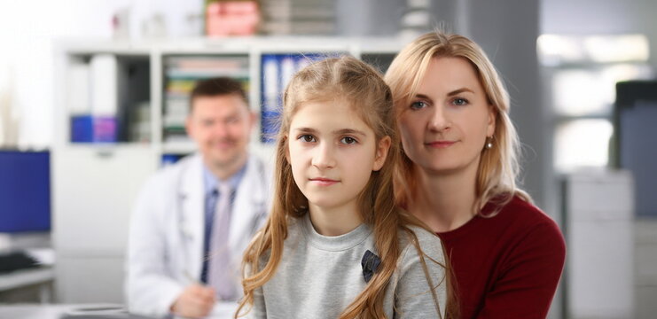 Portrait of mother and daughter on doctors appointment, medical worker smile behind. Need for qualified advice and professional help. Family doctor concept