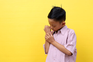 Asian little kid scratching itch hand from a mosquito bite at studio shot isolated on yellow...