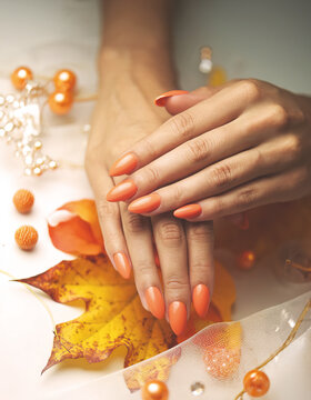 Sc&ouml;ne und gepflegte Frauenh&auml;nde mit orangen Gel-Fingern&auml;geln und Herbstdeko