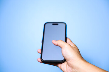 Closeup of hand holding or using smartphone on blue background.