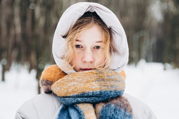 Teenage girl wrapped in warm clothes in snowy forest