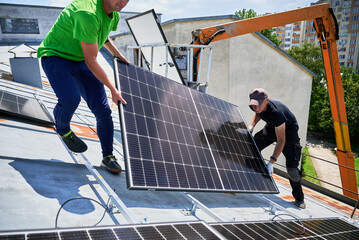 Workers building solar panel system on metal rooftop of house with assistance of crane lift. Two...