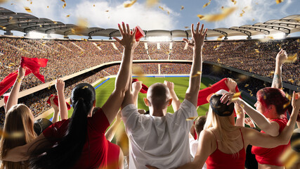 Vibrant soccer stadium scene filled with fans waving red flags and cups, with bright confetti falling around them, as sun shines over field. Concept of sport evens, championship, celebration, victory.