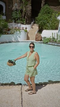 Woman enjoying the pool at lagomar lanzarote canary island wearing sunglasses and holding a straw bag against a rocky background with green foliage and cascading water in the serene setting