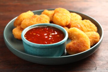 Plate with hot chili sauce and nuggets on wooden table, closeup