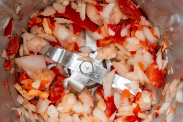 Chopped garlic, onion, and red bell pepper inside a food processor, ready for cooking. Fresh ingredients prepared for a flavorful dish, vibrant and colorful kitchen scene.