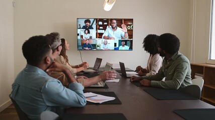 A lively and productive team meeting is captured where colleagues are connected via a large screen, showcasing a blend of in-person and remote collaboration. Virtual meeting concept
