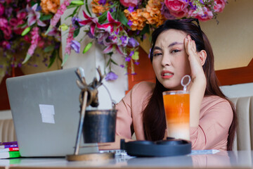 expression of beautiful young asian woman looking at camera holding her head in her arms, headache vertigo sitting on the sofa in an indoor coffee shop. for health, lifestyle, education, advertising