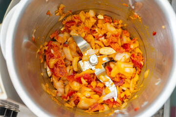 Chopped garlic, onion, and red pepper cooking in a food processor with coconut milk and curry, ready for a delicious recipe. Vibrant colors and fresh ingredients captured in action.