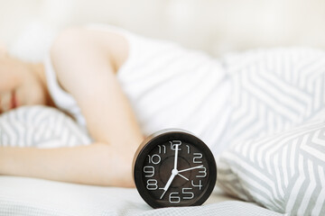 Alarm clock on bed. Kid boy teenager sleeping on the background.