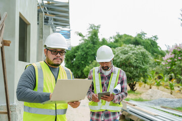Asian male engineers at a construction site. working on a laptop, reviewing project plans on a...