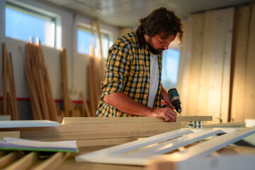 Caucasian carpenter in a workshop drilling a hole on a piece of wood.