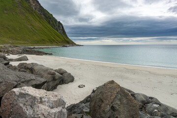 Sandy beach with stones and camping fireplace and mountains in cloudy background, Lofoten Norway