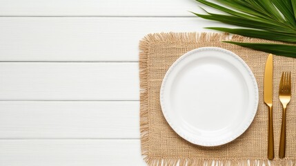 This stylish table setting features a beige plate and golden cutlery on a white linen placemat, accented with lush tropical palm leaves, perfect for a chic dining experience