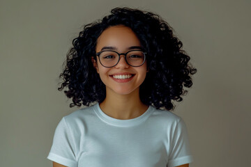 Cute, smiling young woman with curly black hair, glasses, and a white t-shirt.