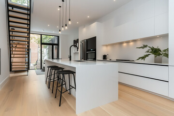 Fototapeta premium A clean, minimalist open-concept kitchen with white quartz countertops and sleek handleless cabinetry. The central island features a waterfall edge design, while the matte black bar stools offer a sub
