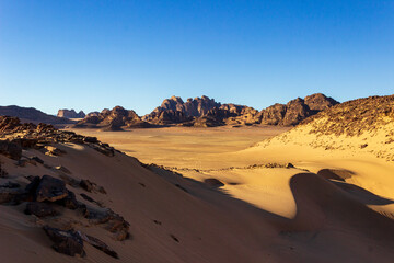 Fototapeta premium A stunning view of the sand dunes and unique rock formations in the Jordanian desert, capturing the dramatic landscape under the clear blue sky