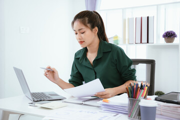 Confident Asian businesswoman in her office checking financial reports on her laptop. Analyzing data, planning strategies and full of success, professionalism and entrepreneurial spirit.