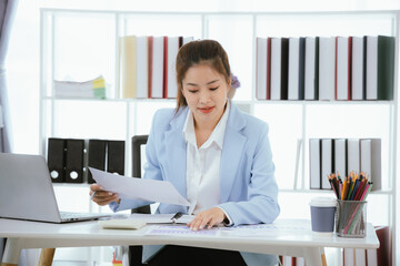 Confident and charming Asian businesswoman using laptop and smartphone. She is full of...