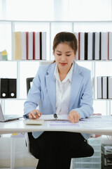 An Asian businesswoman works at her desk in an office. She works hard on her laptop, communicates online, manages her tasks, and easily balances her career.