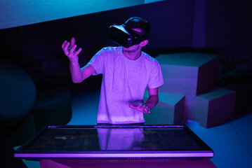 Young man interacting in a digital world, using virtual reality headset with motion tracking tech, making hand gestures in the air.